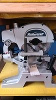 Front view of Mastercraft compound mitre saw showing blade guard with brand logo and mounted wooden base.