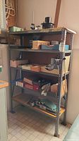 Full view of the assembled five tier metal shelving unit with various boxes and items on shelves (contents not included)