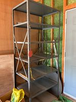 Full front view of tall gray metal shelving unit showing all five shelves and base. Shelf unit is located in unfinished garage space.