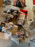 Photo showing multiple boxes containing paint spray guns, metal paint containers, paint scrapers, rollers, and various accessories scattered on concrete floor.