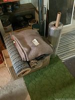 Photo showing rolled runners, folded wool blanket on cardboard box, green scatter rug on floor, and roll of underlay with bubble wrap