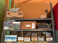 Wide shot of shelving unit with boxes of labeled nuts, bolts, springs, and other hardware items plus packaging material and mesh rolls