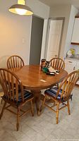 Dining table with four spindle back chairs surrounding it. Chairs have blue and white striped seat cushions. Table is medium oak finish with turned pedestal base.