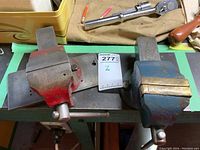 Top view showing red and blue metal bench vises mounted on a bench surface with tools around.
