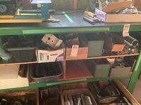 Metal punchers, shapers, and various pipes and angle irons organized on green metal shelving