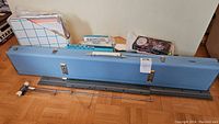 Closed light blue carrying case behind main needle beds and accessories on parquet floor