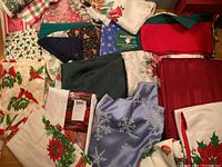 Overview of multiple Christmas table linens in various patterns including poinsettias, cardinals, holly, and snowflakes.