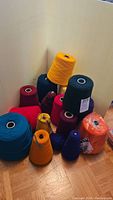 Various large cones of yarn in colors including yellow, navy blue, red, orange, and others gathered in a corner on the floor.