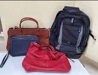 Four bags on white surface: brown leather bag, dark blue leather clutch, red leather shoulder bag, black Samsonite knapsack