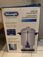 Photo of the Delonghi coffee urn box showing the product image, capacity, adjustable thermostat feature, and coffee level indicator.