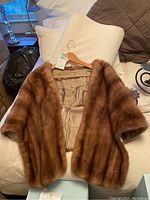 Fox fur stole/shawl laid out flat showing brown fur exterior and beige satin lining on a bed.