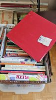 Photo showing a box filled with assorted knitting and crochet books, some titles visible on the top layer.