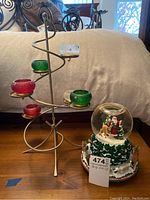 Overview of candle holder and snow globe side by side on a wooden table near a bed.