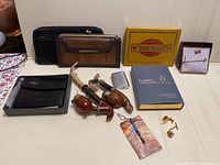 Full lot display showing pipes, lighters with box, wallets, cigarette tin, tie clips, and pins arranged on table