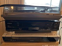 Stack of three electronic devices: JVC turntable on top, Hitachi VCR middle, Toshiba DVD recorder bottom