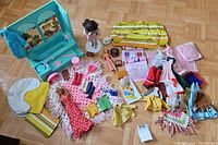 Wide view of lot contents including Barbie dolls, various doll clothes, shoes, accessories and turquoise furniture piece.