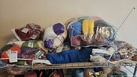 Multiple bags and skeins of assorted yarn displayed on a metal rack, including plastic sealed bags of yarn and loose skeins.