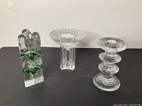 Three Scandinavian glass candle holders displayed on a black surface against a white wall.