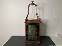 Full view of antique stained glass hall lantern lamp showing entire lamp with metal handle and frame on a black surface.