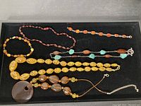 Full view of the collection in a black tray, showing various yellow amber beads necklaces, a turquoise combination necklace, and dark amber beads.