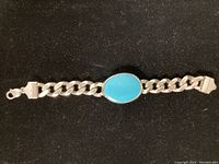 Full view of the sterling silver Cuban link bracelet with oval turquoise stone centerpiece on black background.