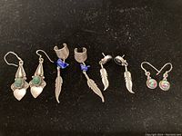 Four pairs of Navajo sterling silver earrings placed on black felt showing various designs with stones and feathers.