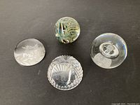 4 art glass paperweights arranged on a surface showing variation in shape and design.