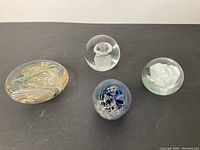 Four art glass paperweights shown together on a flat surface.