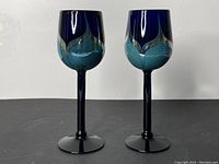 Pair of cobalt blue art glass wine glasses with detailed feather-like hand-painted design.