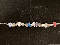 Full length view of the bracelet showing multiple beads including glass and silver ones, spaced along a sterling silver woven chain.