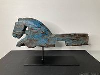Side view of the carved wooden horse showing bluish paint wear and prominent banded neck carve.