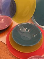 Close up image showing various coloured bowls and plates stacked, highlighting bright hues of blue, orange, pink, yellow, teal, and lime green.