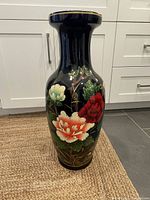 Front view of a large black oriental floor vase with vibrantly colored flowers in red, orange, white, and green.