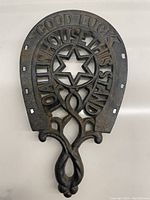 Full front view of the antique iron trivet showing its horseshoe shape, central star cut-out, and raised motto text