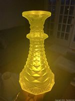 Front and angled view of the glowing yellow-green Vaseline uranium glass vase showing its textured pointed tiered cut design and flared rim.