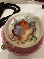 Close-up of fine bone china cup and saucer with hand-painted fruit design and gilt detail