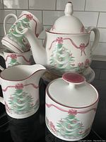 Full view of the Christmas tea set with two mugs stacked inside each other, teapot, creamer, and sugar bowl with lid arranged on kitchen counter against tiled backsplash.