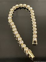 Full view of the gold-tone tennis bracelet with round clear stones laid in a curved formation, clasp visible.