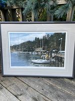 Full view of framed lithograph depicting a harbour with boats, docks, and wooded hills under a partly cloudy sky.