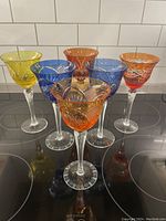 Six hand-cut crystal colored wine stems grouped on black surface showing assorted vibrant colors and unique cut designs.