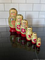 Photo showing full set of six hand painted traditional nesting dolls in decreasing sizes, standing on a reflective black surface with white tiled background.