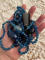Photo of strand of faceted blue turquoise beads with black onyx rectangular and square beads and other agate stones held in hand on fabric background