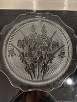Top view of clear depression glass cake plate showing floral iris design embossed in the center, scalloped edge around rim