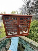 Closed wooden jewelry box with two glass-paned doors and decorative wooden grille on each door.