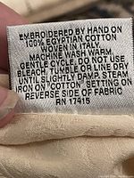 Care label indicating hand embroidery on 100% Egyptian cotton, woven in Italy, washing instructions