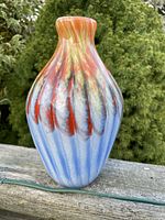 Front and side view of 9 inch tall cased art glass vase with a blend of blue, orange, yellow, and white colors over white base outdoors