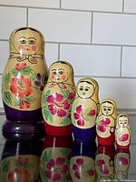 Set of five wooden nesting Matryoshka dolls arranged largest to smallest, showing hand-painted floral designs and colored bases.