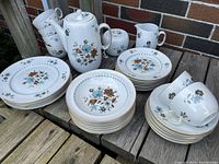 Wide view of entire porcelain set showing cups, saucers, plates, bowls, coffee pot, creamer, sugar bowl, all with floral pattern and gold rim detail