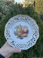Front view of the porcelain bowl showing the painted fruit and nut design on the inside with pierced lattice edge and floral accents.