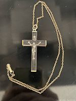Photo of crucifix necklace with a dark cross that is possibly ebony, detailed metallic figure of Christ, and an 18-inch metal chain with clasp laid out on a black surface.